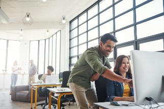 Two safety colleagues in a bright office laughing and looking at a computer